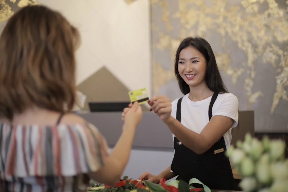 A smiling cashier accepting a credit card payment from a customer at a retail counter.